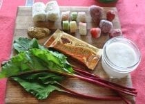 A Mixed Nut Medley BumbleBar is the featured smoothie ingredient on this wooden cutting board with banana, rhubarb, strawberry, almond milk, cashew butter, and beet greens.